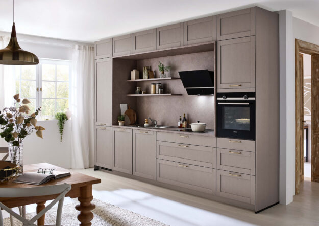 Beige Landhausküche mit Rahmenfronten, integrierten Geräten und offener Nische, kombiniert mit warmen Holzdetails und eleganten Griffen